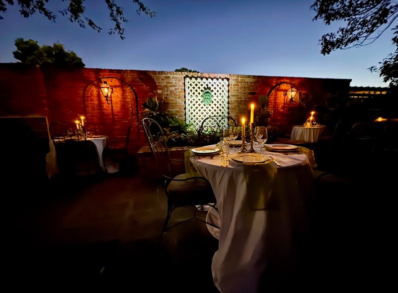 Candlelit dining tables arranged along a historic brick garden wall
