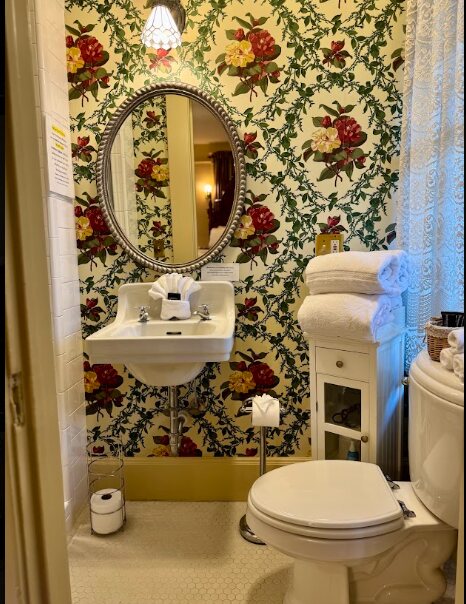 A bathroom with vivid floral wall covering and fresh white towels